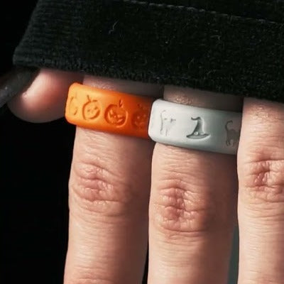 A hand wearing the orange jack-o'-lantern ring and the light gray Spooky Night ring on two fingers